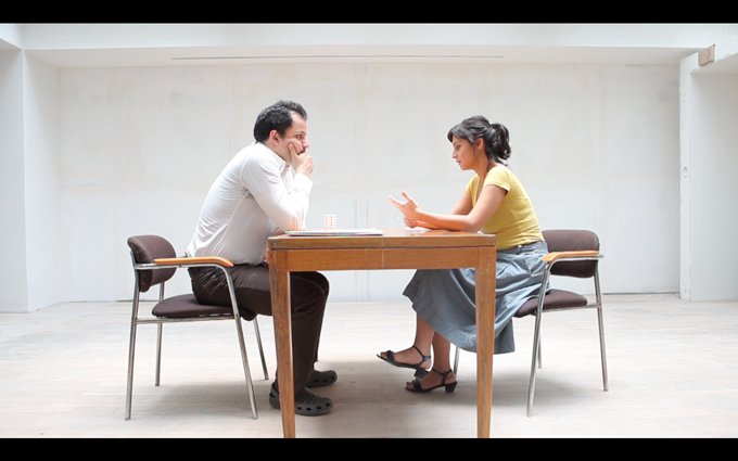 a young man and woman sitting at a table in an empty room