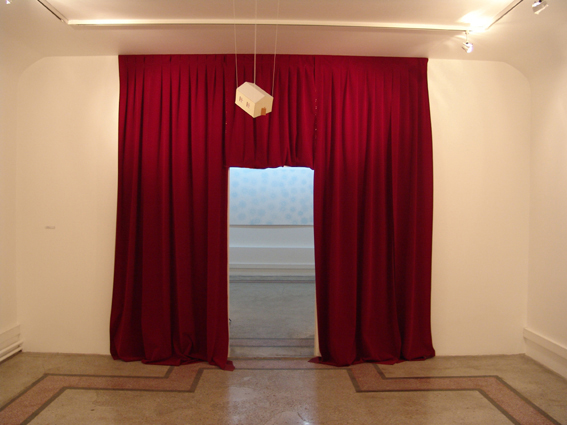 red velvet curtain at the background, there is a cardboard house in the middle of the room 